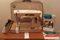 Full setup of Singer Model 403 sewing machine with beige hard case, beige fabric pouch containing motor and cords, original instruction manuals and Singer branded accessory box on a wooden table.