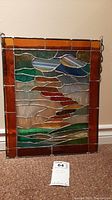 Full view of stained glass panel showing abstract multicolored glass pieces bordered in amber glass and metal soldered frame.