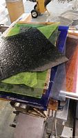 Stack of assorted stained glass sheets with varying textures and colors including green, black, blue, and amber.
