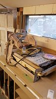 Front and side view of saw on workbench showing metal frame, sliding table, motor, water hoses, diamond blade