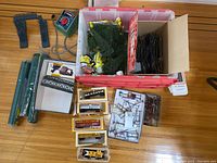 Full overview of train set components including carriages in packaging, bridge parts, track control unit, and various trees in a red bin.