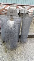 Four tightly wound rolls of metal wire mesh with 3/4 inch square openings, standing upright outdoors on a concrete surface with a brick wall background.