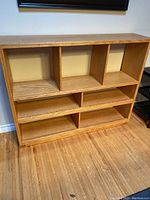 Front view of the wooden bookshelf showing nine open compartments and natural wood finish.