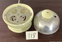 Photo of electric egg cooker base and lid separated, showing cream ceramic base with egg holes and metal dome lid with plastic knob.