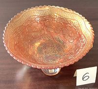 Top-down angled view showing embossed dogwood flower and ribbon pattern inside the golden marigold carnival glass bowl with sawtooth edge.