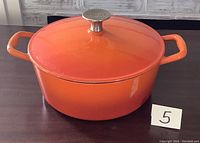 Full view of the round orange enamelled cast iron casserole dish with lid on, showing its shape and handles.