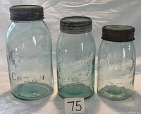 Front view of three vintage Crown glass jars in aqua/green glass, showing embossed logos and metal lids