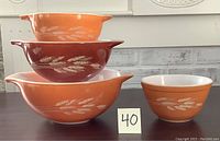 Four Pyrex Cinderella bowls stacked and arranged to show size and color variation. Wheat pattern visible on sides.