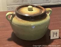 Front and side view of bean crock showing yellow-green ceramic with brown gradient near the lid and two loop handles, placed on a table