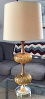 Front view of mid century table lamp showing amber glass globes, teak wood insert, chrome base, and cream lampshade.