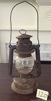 Full view of rusty GSW lantern standing on table showing tall handle, base, and clear glass globe with metal cage.