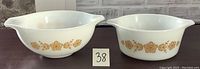 Front view of two white glass Pyrex bowls with gold floral butterfly pattern, showing exterior and handles.