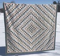 Full view of the large patchwork quilt with a central diamond pattern in shades of green, pink, and white.