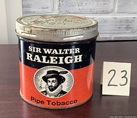 Front view of Sir Walter Raleigh pipe tobacco tin showing red and black label with image of Sir Walter Raleigh and pipe tobacco text.