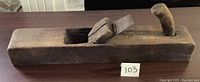 Front side view of old wooden hand plane with handle and iron blade fitted.