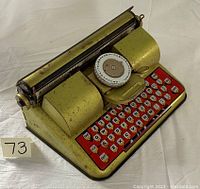 Angled view of vintage yellow tin lithograph typewriter toy showing red keyboard and round dial.