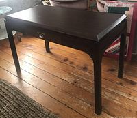 Full view of the vintage wooden table/desk showing tabletop, drawer front with metal pull handle, and four legs on wooden floor.