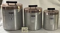 Front view of three vintage aluminum canisters labeled Sugar, Coffee, and Tea with black handles on lids