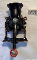 Front view of the cast iron coffee grinder with red handle grip and visible text 'SPONG & CO. ENGLAND' around the wheel.