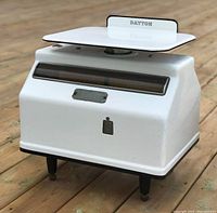 Front view of the vintage enamel Dayton Hobart scale showing the weighing platform, front window, and branding.