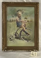 Frontal photo of vintage framed colored picture of boy on tricycle showing frame condition and convex glass.