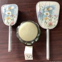 Top view of vanity set showing the floral design on back of mirror and brush and the green glass powder jar with cream lid