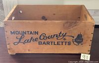 Front side of vintage wooden pear crate showing blue printed text 'Mountain Lake County Bartletts' and pear graphic with 'Lakes'