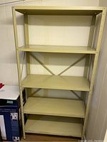 Yellow metal shelving unit with five metal shelves, cross braces on back, sturdy industrial style, with cream yellow paint.