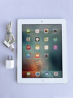 Front view of iPad 2 with screen on, alongside 30-pin USB cable and USB power adapter