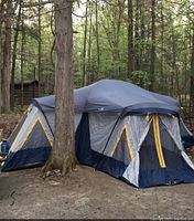 Large assembled camping tent set up outdoors in wooded area demonstrating size and overall condition.