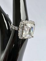Close-up side angle showing the large rectangular cut cubic zirconia center stone and round smaller stones on band and halo setting on silver-tone ring marked 925.