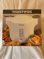 Original boxed packaging of the Toastess deep fryer showing front with product image and main features including safety lid with filter system and warranty information.