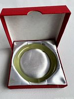Jade bangle placed inside a red square box with white satin interior.