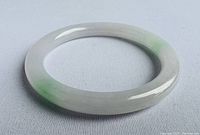 Photo showing the smooth polished jade bangle bracelet with green and white variegated coloring on a light gray fabric background.