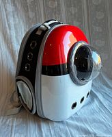 Side angled view showing red, white, and black Pokémon ball design with bubble front window and ventilation holes on the base and side.