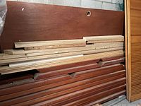 Stack of solid cherrywood boards and molding pieces against a wall, showing reddish-brown finish and various lengths.