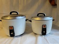 Two large round National brand rice cookers with white bodies and metal lids with black handles.