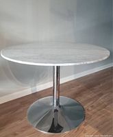 Full view of round marble top table with chrome pedestal base from front angle on wood floor.