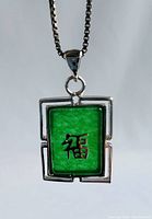 Front view of rectangular green pendant showing silver framed geometric design with Chinese Good Luck symbol cutout.