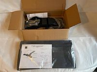 Open box showing mounting bracket with hardware and keyboard tray in plastic wrap with printed installation instructions on top.