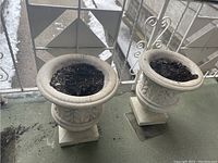 Pair of gray concrete urn planters on balcony with soil inside
