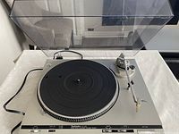 Top-down view of turntable with dust cover open showing platter, tonearm, and power cable