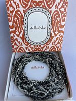 Top view of the original Stella & Dot box displaying the coiled silver hematite lariat necklace inside, showing chain details and branded interior.