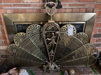 Front view of antique brass fireplace screen showing fan-shaped panels with rays and central figure.