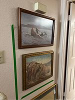 Two framed art prints hanging on wall; top print shows canoe scene, bottom print shows mounted riders.
