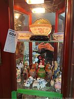 Wide shot showing multiple Asian porcelain items inside a wooden display cabinet, including bowls on stands, Foo dogs, miniature vases and figurines.