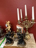 Overview of the ceramic bookends, cherub clock, brass candle stick holders and candelabra on display on a table