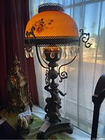 Full view of the vintage bronze lamp with orange frosted glass shade adorned with floral painting and crystal pendants