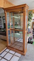 Front view of the wooden curio cabinet showing full height, glass doors and shelves, wood frame, and carved decorative accents.