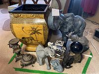 Photo showing assortment of handmade ceramic elephant figurines, yellow planter with elephant designs, and elephant-shaped candle holders and trinket dish.